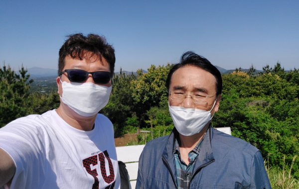 미국에서 사업하는 교민 줄리언 정(왼쪽)이 대수산봉 정상의 강렬한 햇볕에 선글라스를 낀 채 셀카 사진을 찍고 있다. 지평선 왼쪽 끝에 한라산이 솟아 있다. © Julian Chung 