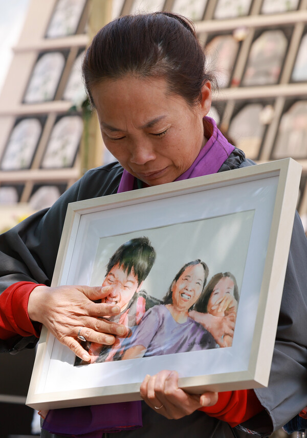 8일 서울 중구 서울광장 이태원 참사 희생자 합동분향소 앞에서 열린 '10.29 이태원 참사 200일, 200시간 집중추모행동 주간' 선포 기자회견에 참석한 한 참사 유가족이 촛불갤러리 작가들이 희생자들과 가족들의 사진을 소재로 그린 '기억 그림'을 품에 안고 손으로 어루만지고 있다. 2023.5.8. 연합뉴스
