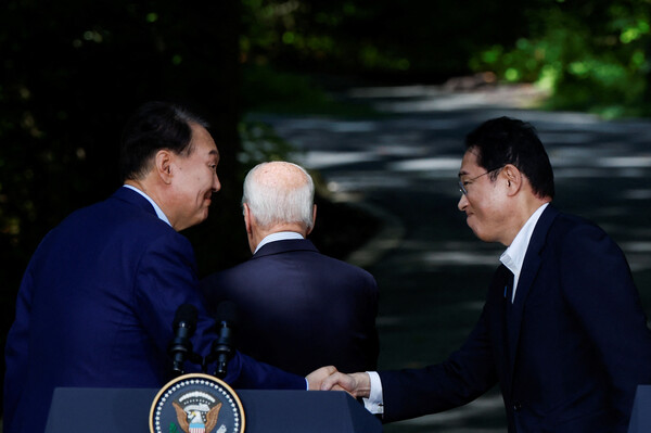 윤석열 대통령(왼쪽)과 기시다 후미오 일본 총리가 18일 미국 매릴랜드주 캠프 데이비드 야외에서 한미일 정상 공동기자회견 끝무렵에 조 바이든 미국 대통령 등 뒤에서 서로 악수를 하고 있다. 2023.8.18. 로이터 연합뉴스 