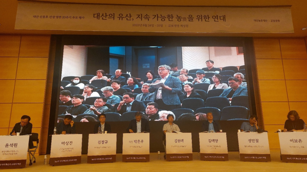 대산농촌재단이 24일 연 ‘지속 가능한 농을 위한 연대’ 심포지엄 종합토론에서 한 참석자가 질문하는 모습이 화면에 비치고 있다. 무대 앞에는 왼쪽부터 발제자 3인과 사회자, 지정토론자들이 앉아 있다. © 이봉수