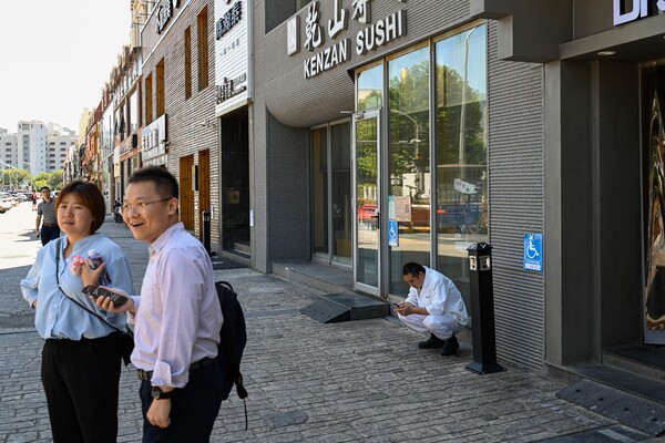 29일(현지시간) 중국 베이징의 한 일식당 밖에서 사람들이 서 있는 가운데 요리사가 쉬고 있다. 중국 해관총서(세관)는 일본이 지난 24일 후쿠시마 제1원자력발전소 오염수(일본 정부 명칭 '처리수') 방류를 개시함에 따라 일본산 수산물 수입을 전면 중단했다. 2023.08.29. AFP 연합뉴스