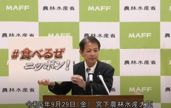 미야시타 이치로 일본 농림수산상이 29일 기자회견에서 "먹고 말거야, 닛뽄!"이란 문구가 적힌 팻말을 들고 가리비 소비를 호소하고 있다. 일본 농림수산성이 배포한 동영상에 나오는 장면이다. 