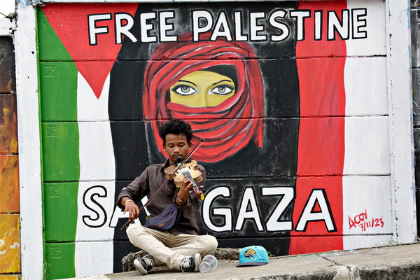 거리의 악사가 8일(현지시간) 인도네시아 데포크의 팔레스타인 해방을 기원하는 벽화 앞에서 바이올린을 연주하고 있다. 팔레스타인 무장정파 하마스의 이스라엘 공격으로 시작된 전쟁으로 팔레스타인에서만 1만여 명이 목숨을 잃었다. 2023.11.8. EPA 연합뉴스