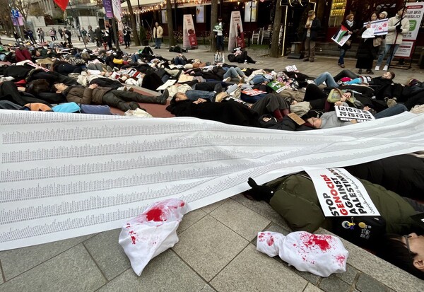 26일 오후 서울 청계천 무교동 사거리 주한 이스라엘 대사관 인근에서 열린 '이스라엘의 가자지구 공격 규탄 한국 시민사회 3차 긴급행동' 집회에 참가한 시민들이 팔레스타인인 희생자를 추모하는 의미에서 죽은 사람들처럼 눕는 '다이-인(Die-in) 퍼포먼스'를 하고 있다. 시민들 위에 긴 펼침막은 팔레스타인 희생자 명단이다. 그 아래 가자지구에서 희생당한 어린이를 상징하는 흰 천으로 덮인 인형이 누워있다. 흰 천에는 피를 상징하는 붉은 색 물감이 칠해졌다. 2023.11.26. 김성진 기자