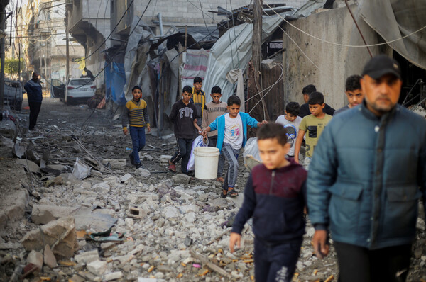 팔레스타인 어린이들이 가자 남부의 칸 유니스에서 이스라엘의 폭격으로 파괴된건물더미 옆을 지나가고 있다. 2023. 12. 06 [로이터=연합뉴스]