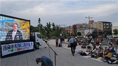 뉴욕주의회 피트 하캄 상원의원이 보내온 지지영상을 집회 참가자들이 보고 있다. 한글 자막과 일본어 자막이 동시에 준비되었다.​​