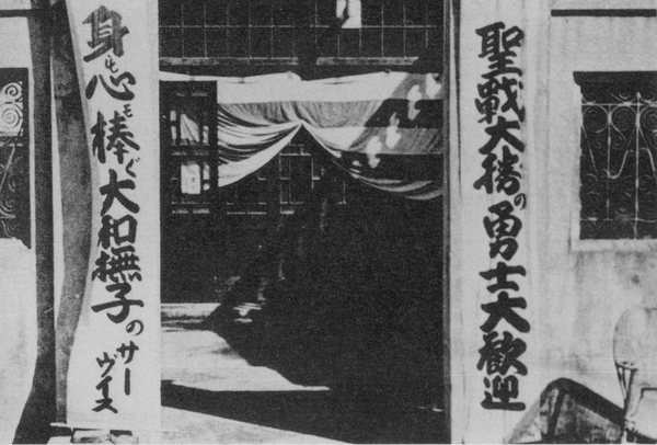 위안소 입구.  오른쪽에 "성전 대승의 용사 대환영", 왼쪽에 "몸과 마음을 바치는 야마토 나데시코의 서비스"라는 문구가 걸려 있다. '야마토 나데시코'는 패랭이꽃인데, 일본여성에 대한 미칭이다.   위키백과 