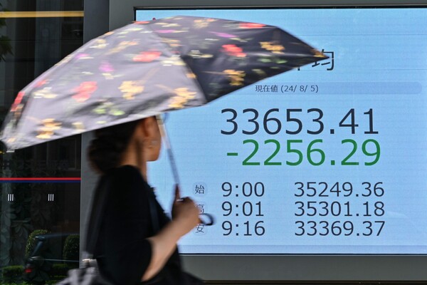 5일 일본 도쿄 시내에서 양산을 쓴 행인이 증시 현황판 앞을 지나가고 있다. 이날 일본 증시 대표 주가지수인 닛케이225 평균주가(닛케이지수)는 장중 7% 넘게 급락하며 약 7개월 만에 최저치로 떨어졌다. 2024.08.05. AFP 연합뉴스