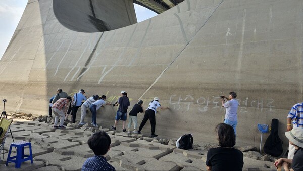 60+기후행동 회원들이 세종보 위를 가로지르는 다리 교각에 분필로 '흘러야 강물이다' '담수 안돼 절대로' '가자 바다로' 등의 글귀를 함께 쓰고 있다.