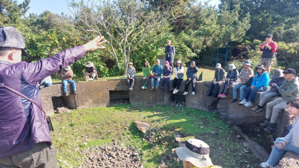 답사자들이 고사포진지 콘크리트 옹벽에 걸터앉아 김현우 사무국장의 설명을 듣고 있다. 네모난 구멍은 연쇄 폭발을 막으려고 분리설치한 탄약고들이다. © 이봉수