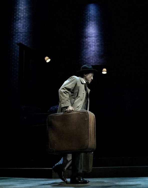연극의 프롤로그, 윌리 로먼이 여행 가방을 들고 무대를 가로지르는 장면. 삶의 무게를 극적으로 보여준다. 어두운 조명 아래 고개를 숙인 모습은 자본주의 체제 속에서 소모되고 버려진 한 인간의 초상이다. 사진=쇼앤텔플레이, T2N 미디어