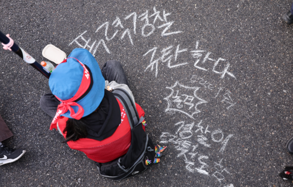 26일 서울 종로구 자하문로에서 경찰들이 전국농민회총연맹(전농) 소속 트랙터를 둘러싸고 있는 가운데 한 시민단체 회원이 아스팔트 바닥에 경찰 규탄 문구를 적고 착석해 있다. 2025.3.26. 연합뉴스