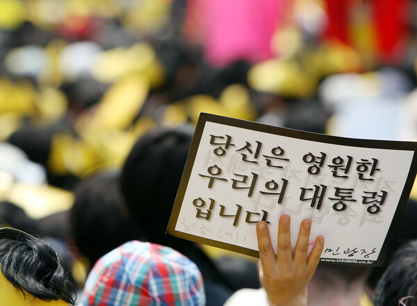 29일 오후 서울 시청광장에서 열린 故노무현 전 대통령의 노제가 끝난 뒤 한 시민이 자신의 마음이 담긴 문구가 세겨진 종이를 들며 화장장으로 떠나는 장례행렬을 지켜보고 있다. 2009.5.29. 연합뉴스