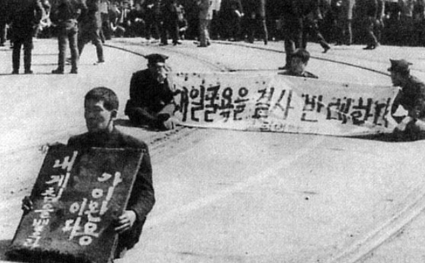 6·3 항쟁 당시 시위대가 ‘대일굴욕을 결사 반대한다’라고 적힌 플래카드와 ‘내게 침을 뱉으라, 내가 이완용이다’라고 적힌 피켓을 들고 있다.