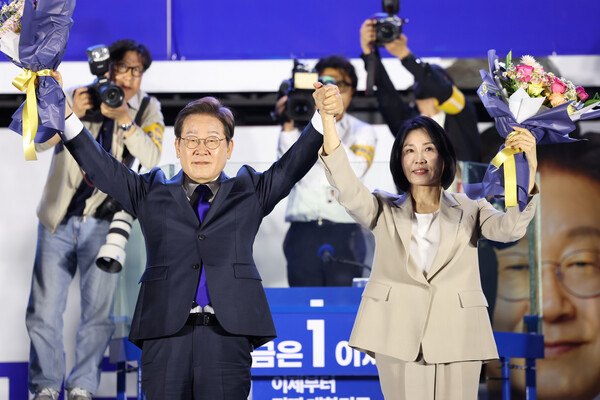 제21대 대통령 당선이 확실시되는 더불어민주당 이재명 대선 후보와 부인 김혜경 여사가 4일 서울 여의도 국회 인근에서 당 주최로 열린 국민개표방송 행사에 참석해 꽃다발을 받고서 시민들을 향해 두 팔을 들어올려 인사하고 있다. 2025.6.4 [공동취재]  연합뉴스