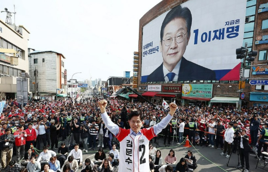 국민의힘 김문수 대선 후보가 5월 14일 경남 밀양시 밀양관아 앞에서 유세하고 있다. 뒤편 건물에는 더불어민주당 이재명 대선 후보의 사진을 담은 대형 플래카드가 걸려 있다. 2025. 5. 14 연합뉴스