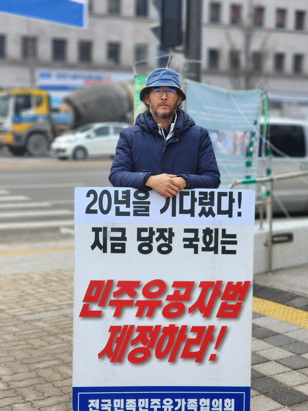 한현우 실장이 '20년을 기다렸다. 민주유공자법 제정하라'라는 피켓을 들고 국회앞 1인시위를 하고 있다.
