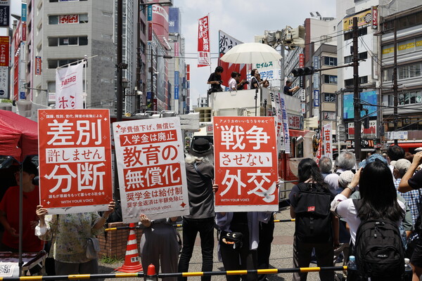 7월 3일, 일본 도쿄에서 열린 7월 20일 참의원 선거를 위한 일본 공산당의 거리 유세 연설에 사람들이 모여 있다. 7월 20일 일본 참의원 선거를 위한 선거 운동이 이날 시작되었으며, 이는 이미 주요 지방 선거에서 패배를 경험한 이시바 시게루 총리의 소수당 정부에 새로운 시험대가 될 것이다. 플래카드에는 (왼쪽부터) "차별과 분열은 용납되지 않는다", "무상 교육", "전쟁을 막는 외교"라고 적혀 있다. 2025.7.3. EPA 연합뉴스